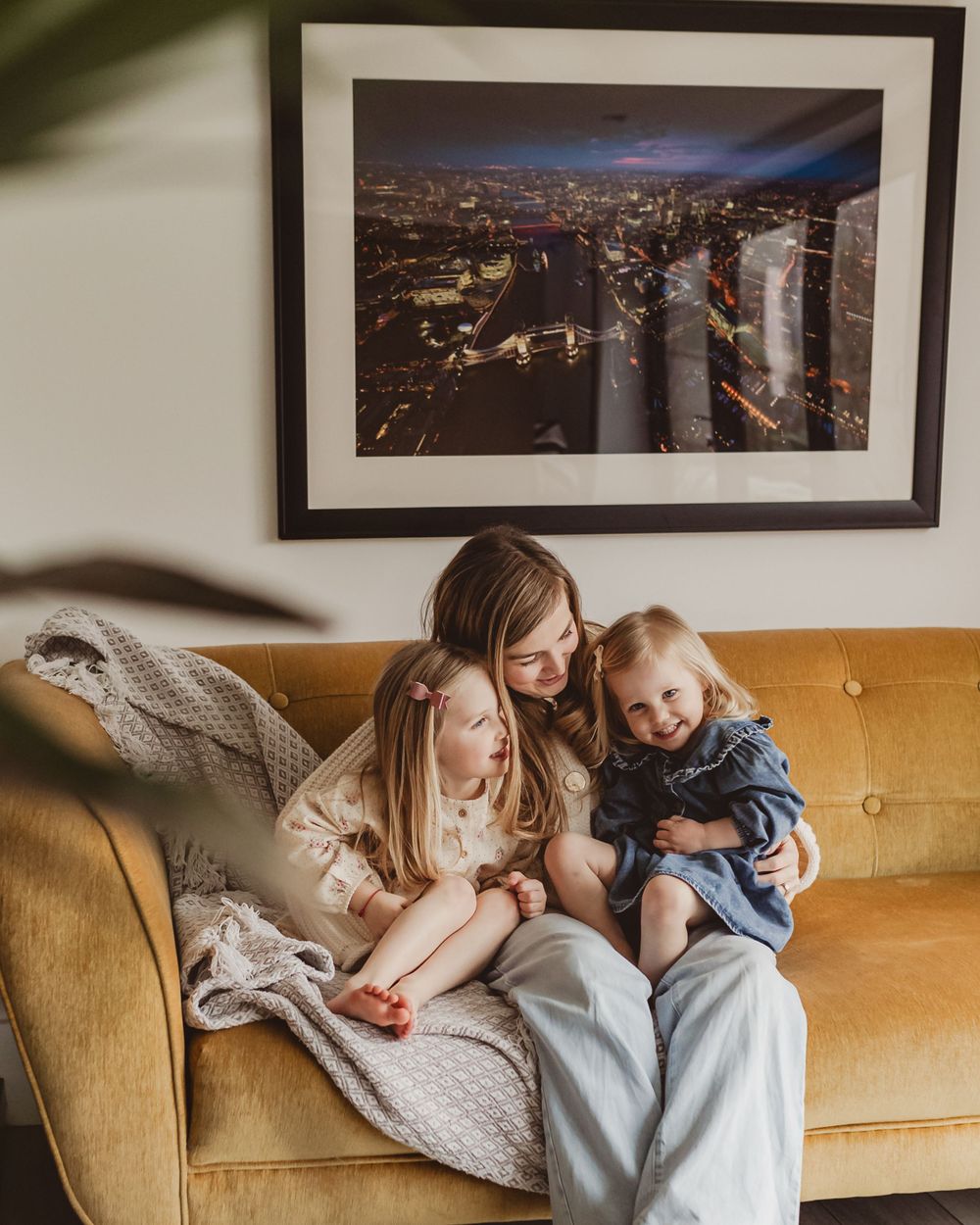 Woman and two little girls sharing a joyful moment on a mustard velvet sofa at home.