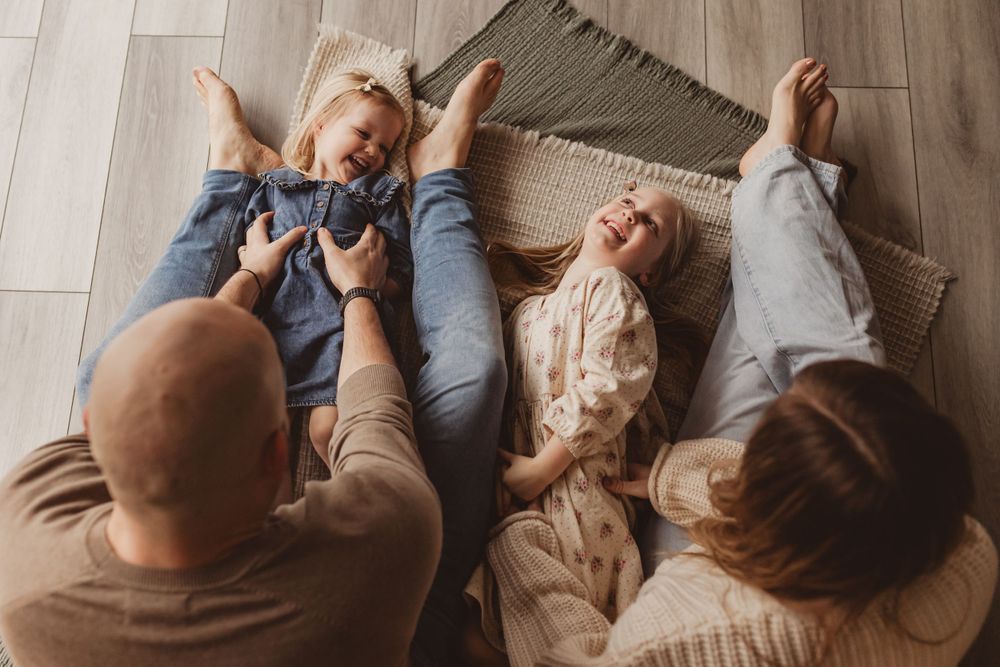 Overhead view of parents playing with two laughing children lying on a floor rug.