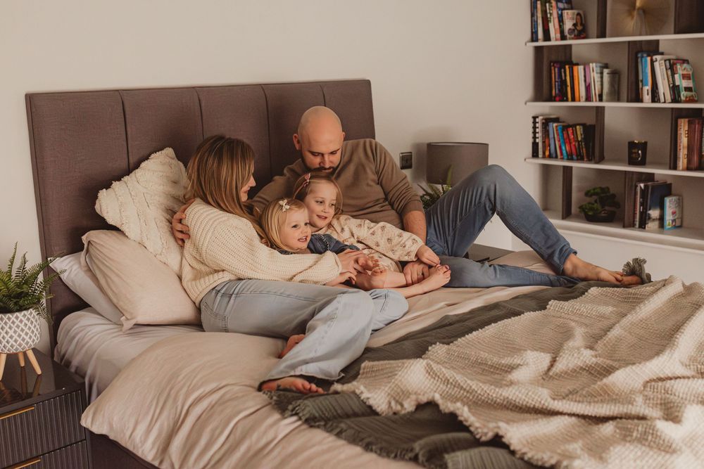 Family of four cuddling together on a large bed in a cozy modern bedroom.