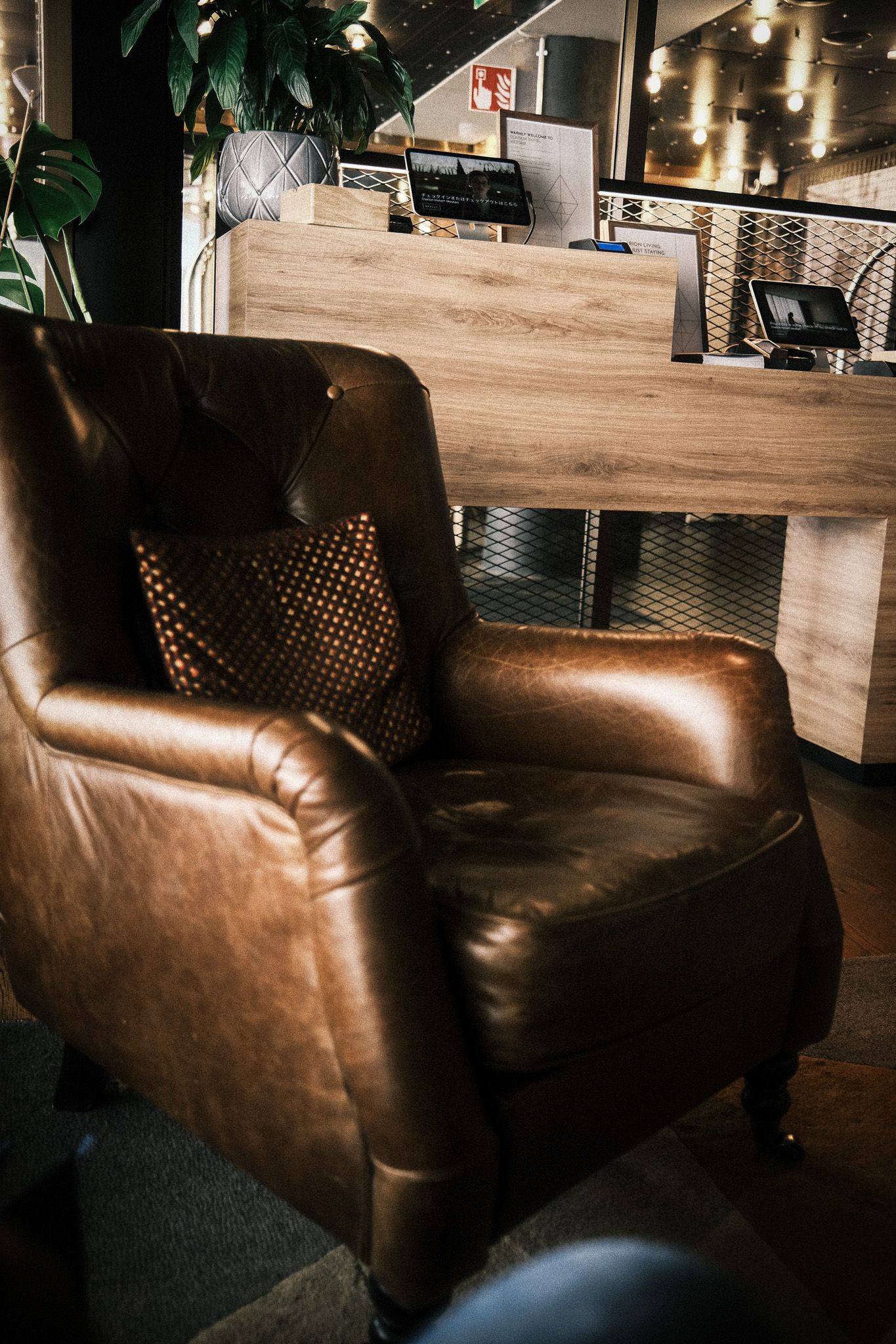 A luxurious brown leather armchair with a decorative pillow sits beside a wooden reception desk in a modern interior.