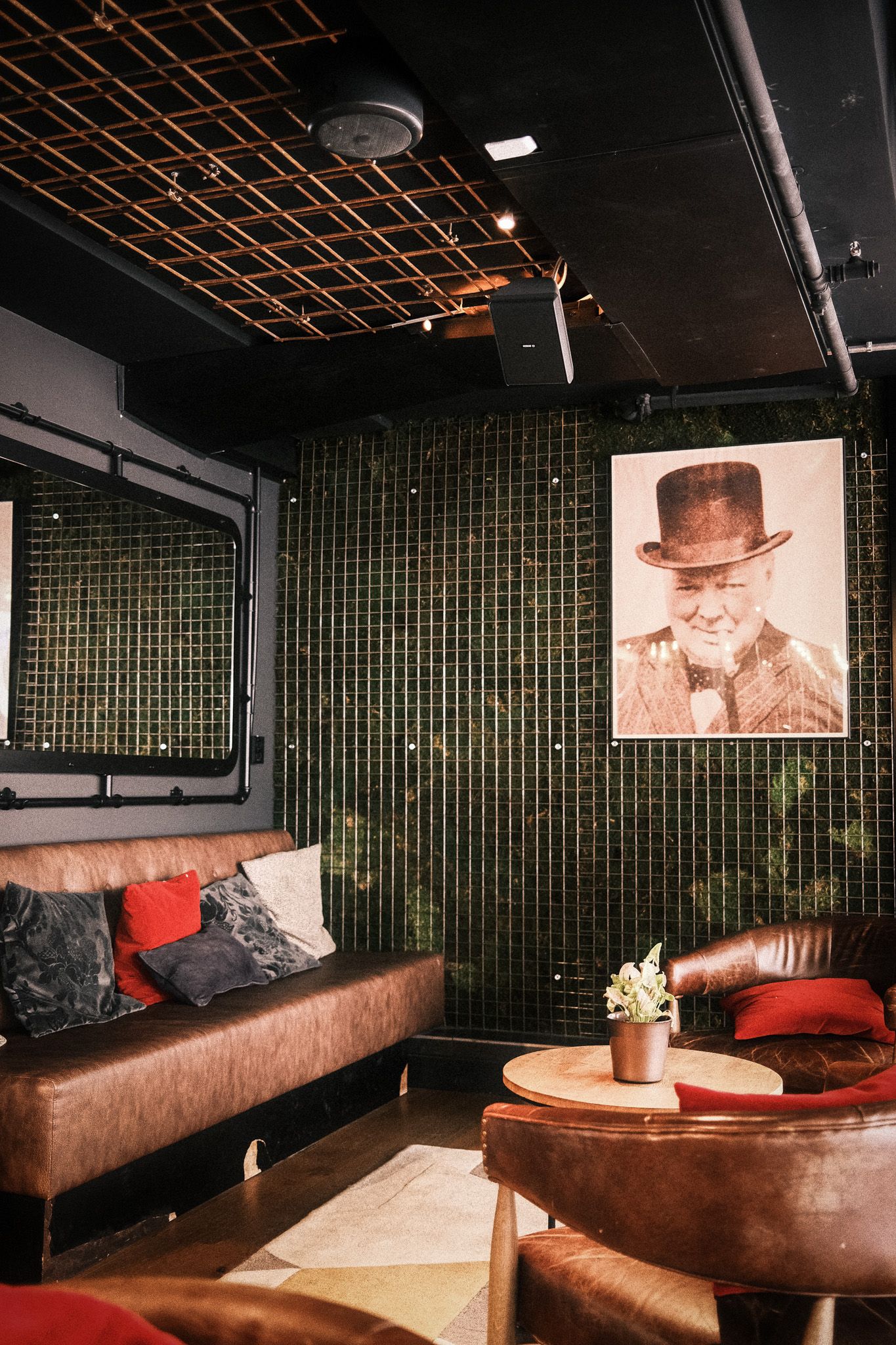 Upscale lounge with green mosaic tiles, leather sofas, red pillows, and a vintage portrait painting on the wall.