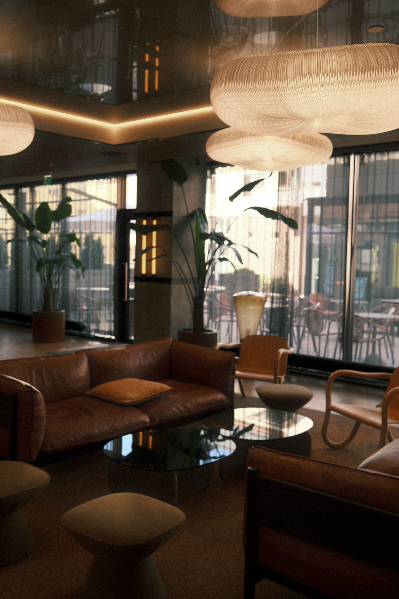 Elegant hotel lobby with brown leather sofas, glass coffee tables, large pendant lights, and tropical plants near floor-to-ceiling windows.