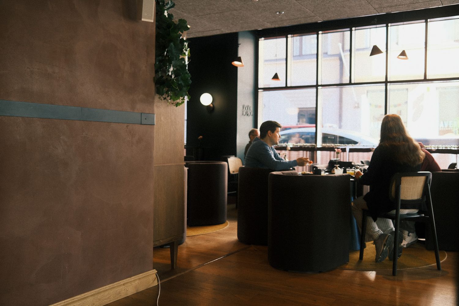 People dining in a modern restaurant with large windows, dark furniture, and contemporary decor.