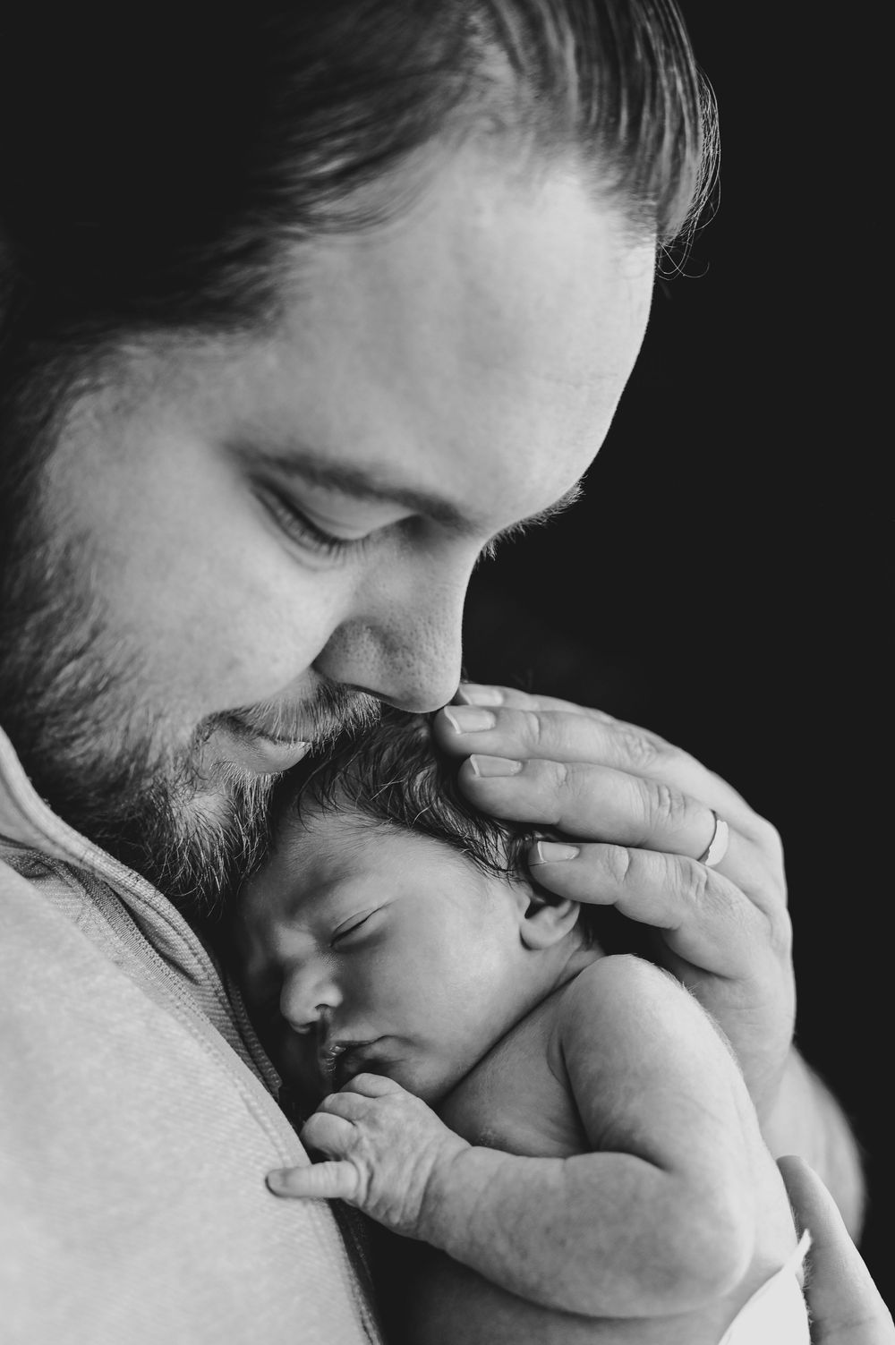Black and white photo of a bearded father tenderly holding and nuzzling his sleeping newborn baby.