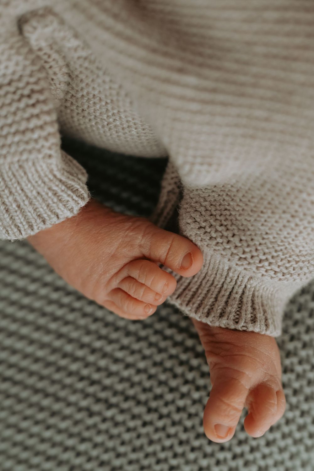 Close-up of tiny newborn baby feet and toes wearing a soft knit cream sweater on a mint green blanket.
