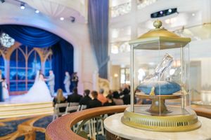 Cinderella glass slipper display case at a Disney wedding venue with elegant blue curtains and ceremony in background.