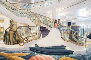 Bride and groom embrace on an elegant cruise ship staircase with gold railings and ornate bronze statue.