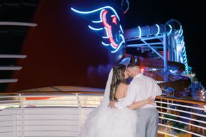 Bride and groom sharing a romantic kiss on a Disney cruise ship deck at night with glowing neon lights.