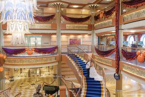 Elegant cruise ship atrium featuring grand staircase, ornate columns, and colorful draping decor.