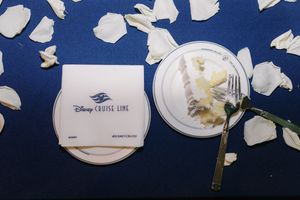 Disney Cruise Line branded napkin and plate with fork on navy blue tablecloth scattered with white rose petals.