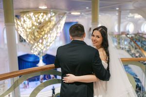 Bride and groom sharing a romantic moment on an elegant staircase with sparkling chandeliers in a grand wedding venue.