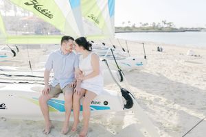 Couple sitting together on a sailboat on a sandy beach, smiling at each other in a romantic outdoor setting.