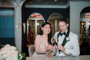 Couple in formal wedding attire toasting with champagne glasses, smiling joyfully at elegant venue reception.