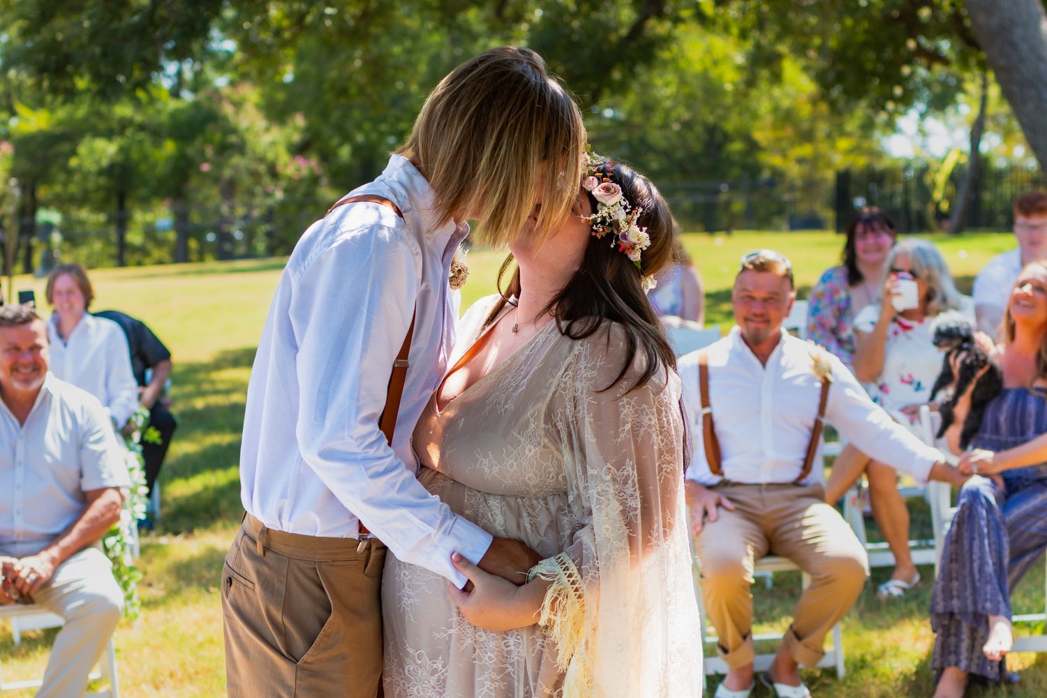 Newlywed couple exits stone church venue in wedding attire, surrounded by smiling guests celebrating their marriage.