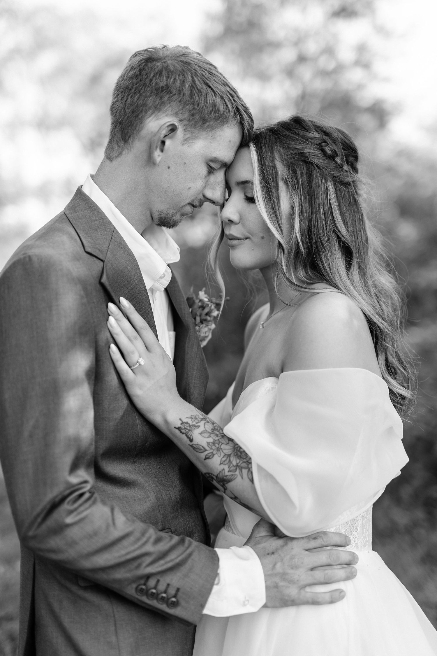 A bride and groom share a romantic moment outdoors, with the bride in an off-shoulder gown holding a floral bouquet.