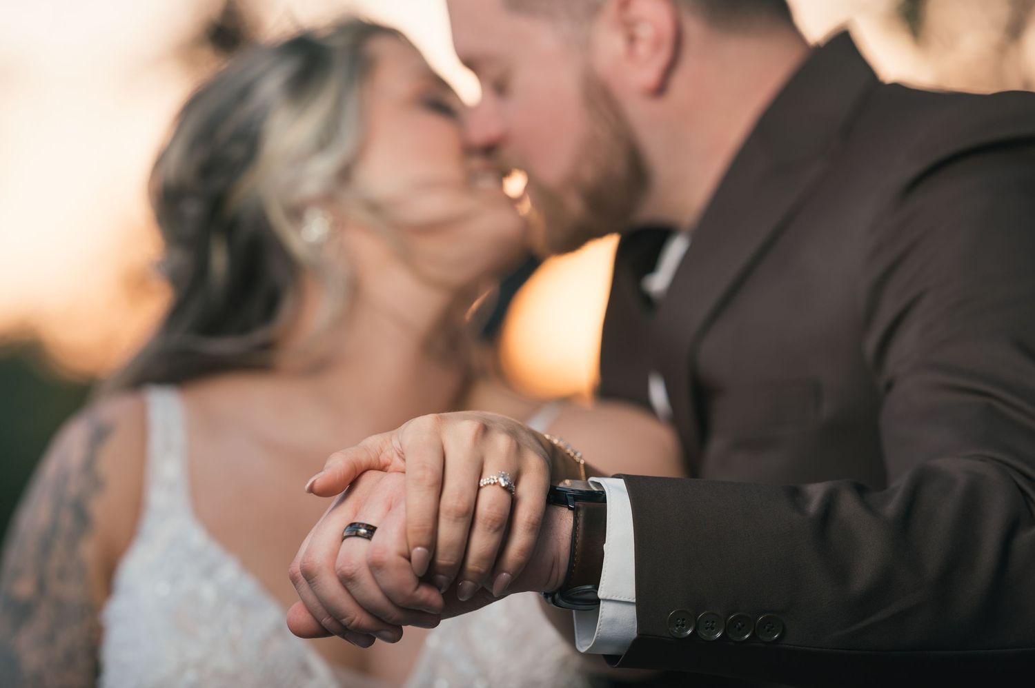 Newlywed couple kissing at sunset while showing off their wedding rings in a romantic portrait.