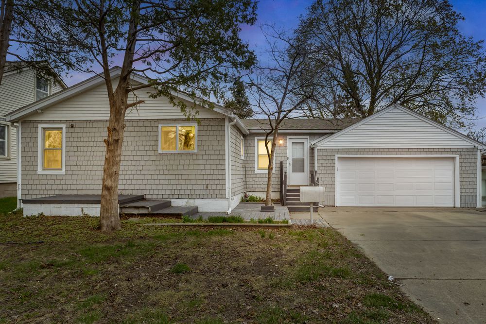 Charming ranch-style home exterior with shake siding, attached two-car garage, and mature trees at dusk.