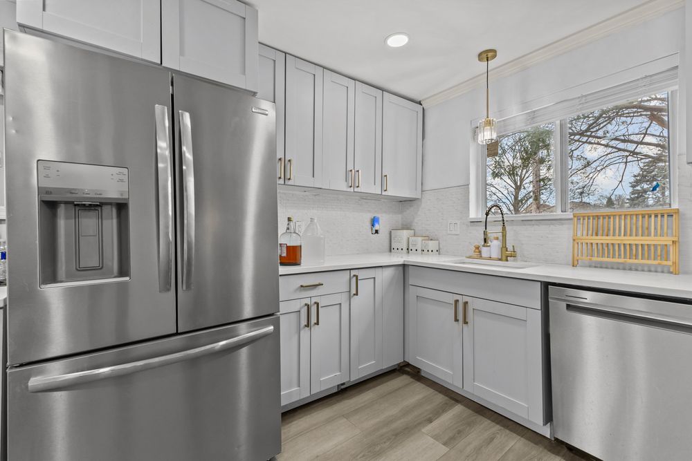 Modern kitchen with gray shaker cabinets, stainless steel appliances, white quartz countertops, and pendant lighting.