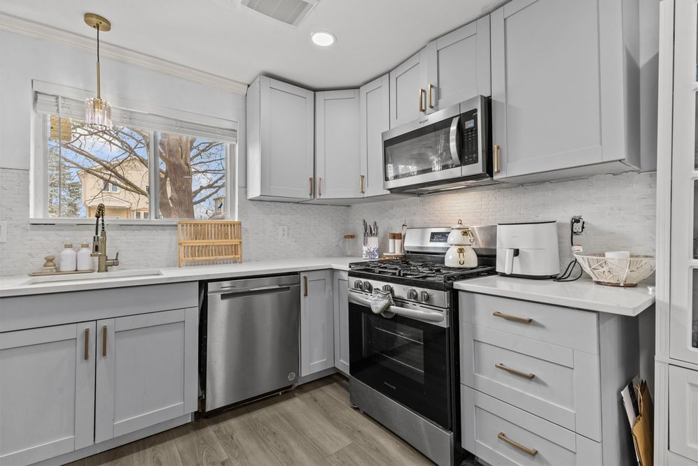 Bright kitchen with gray cabinets, stainless steel appliances, subway tile backsplash, and gold pendant lighting.