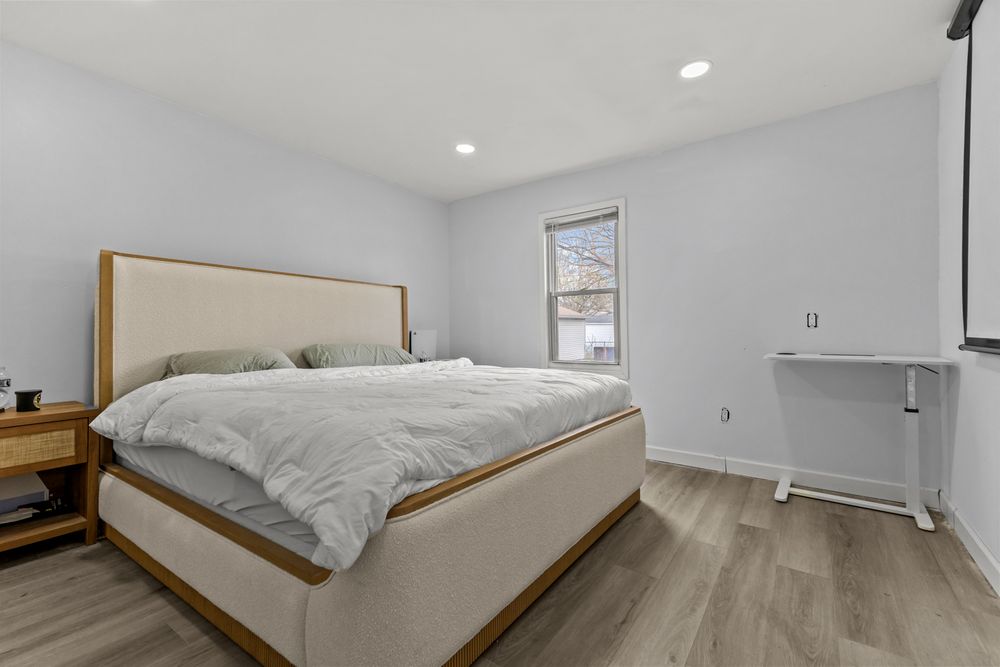 Bright minimalist bedroom with upholstered bed frame, hardwood floors, and recessed lighting.