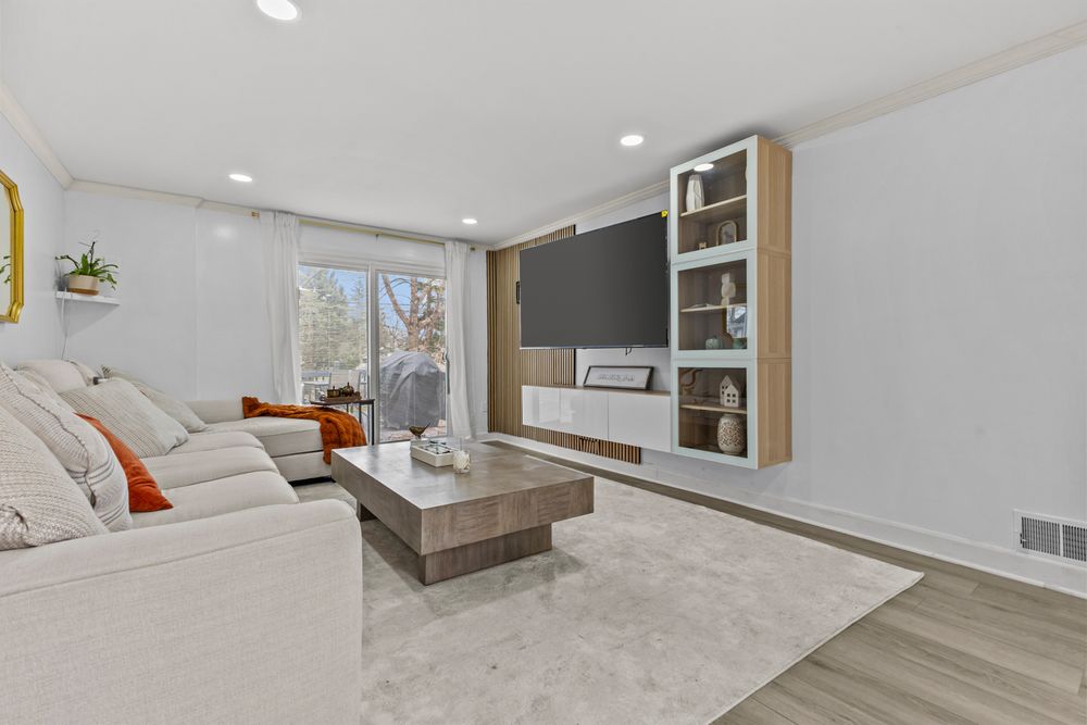 Contemporary living room with gray sectional, wall-mounted TV, built-in shelving, and light hardwood floors.