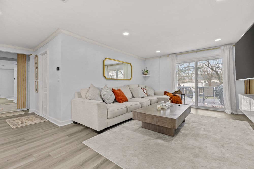 Spacious living room featuring beige sectional sofa, orange pillows, sliding glass doors, and light hardwood floors.