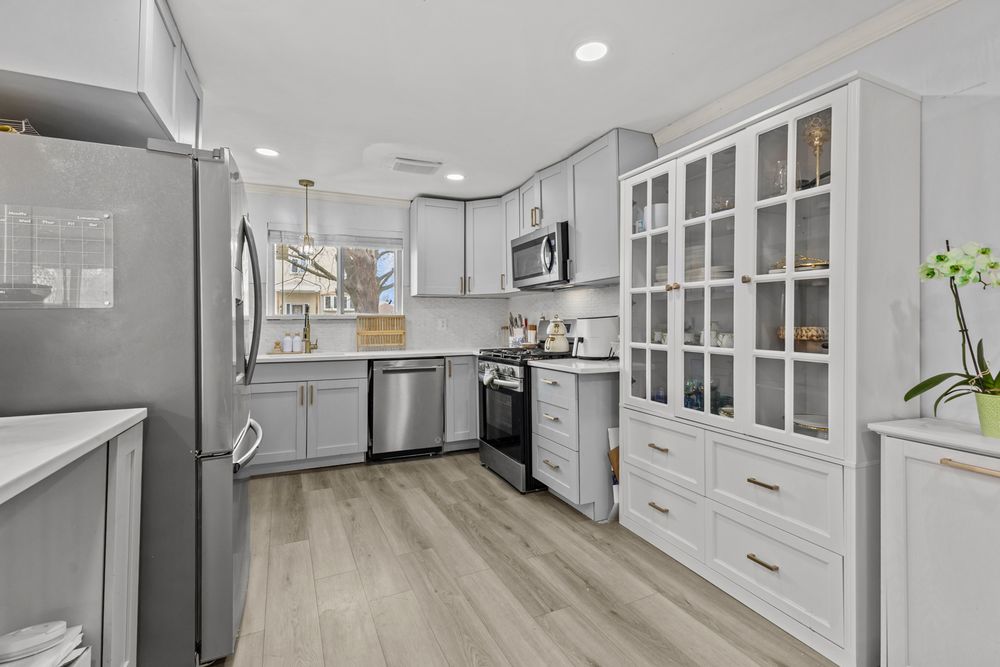 Modern kitchen with gray cabinets, stainless steel appliances, glass-front display cabinet, and light hardwood floors.