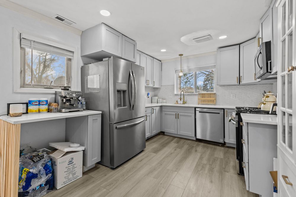 Updated kitchen featuring gray cabinets, stainless steel refrigerator, dishwasher, and bright natural light from windows.
