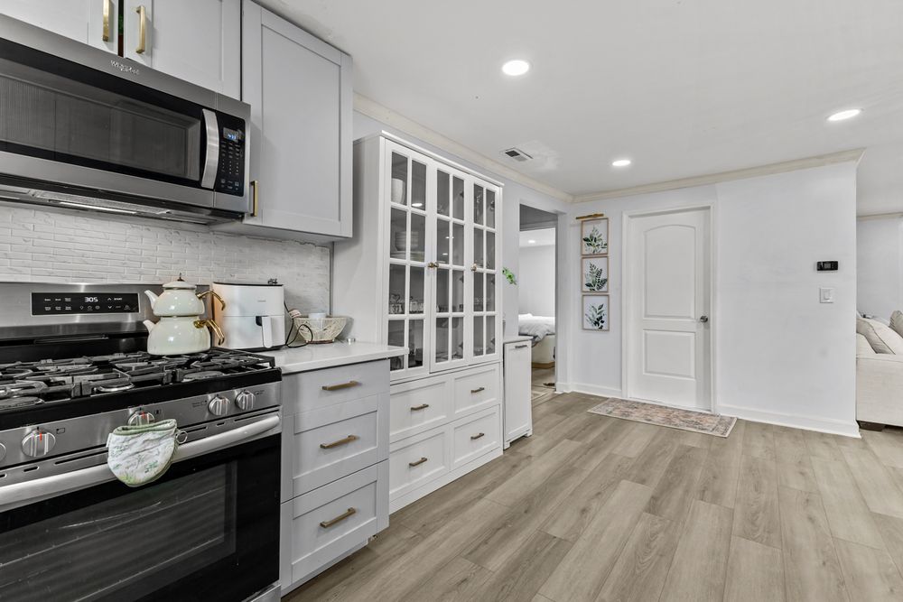 Contemporary kitchen with gray cabinets, stainless steel gas range, microwave, glass-front cabinet, and wood-look floors.