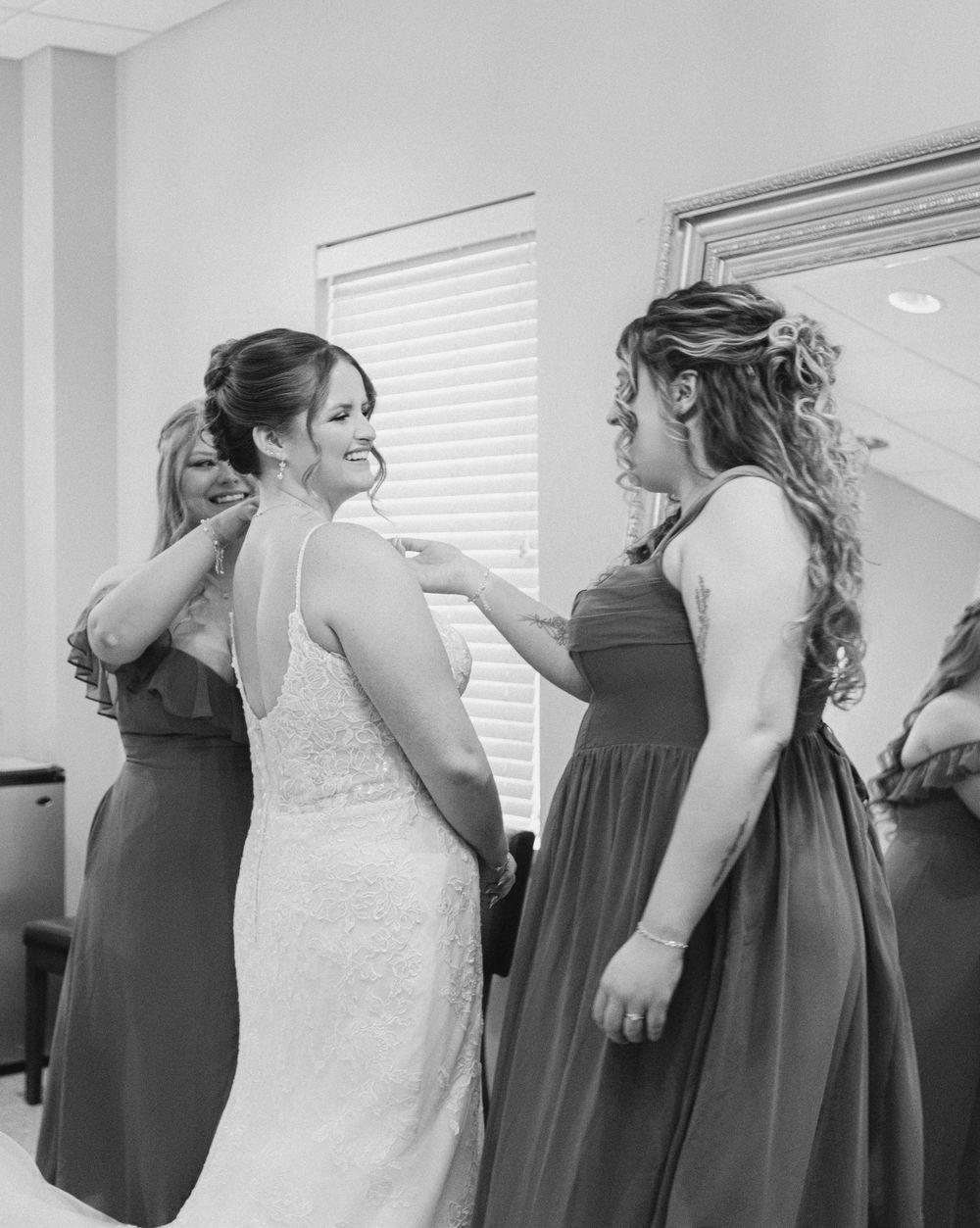 Black and white photo of bridesmaids helping bride into her lace wedding gown before the ceremony.