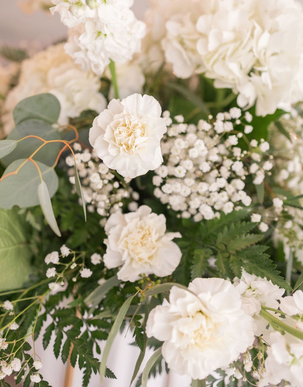 Elegant wedding floral arrangement featuring white carnations, baby's breath, and eucalyptus greenery.