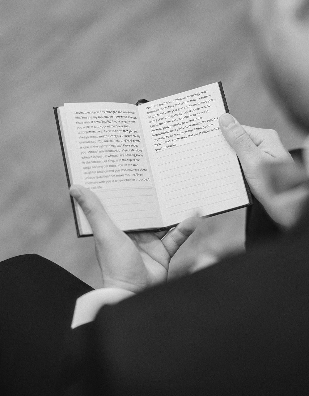 Groom reads handwritten vows from small notebook during wedding ceremony in black and white photo.