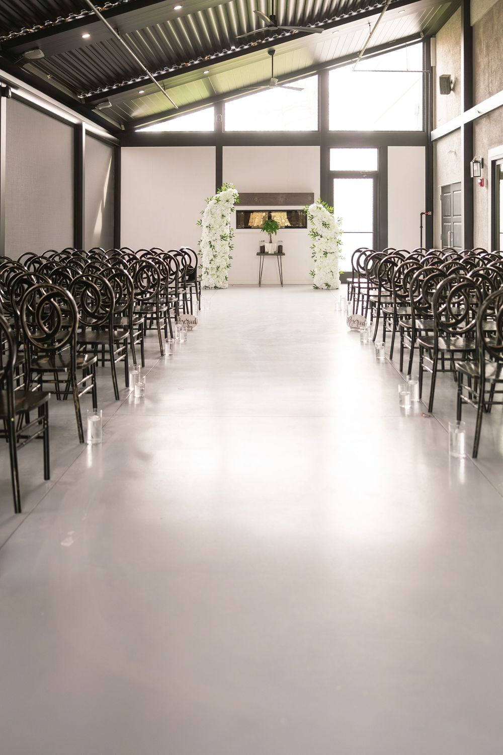 Elegant wedding ceremony venue with rows of dark chairs, white aisle, and floral arch at the altar. brookshire wedding venue Delaware ohio