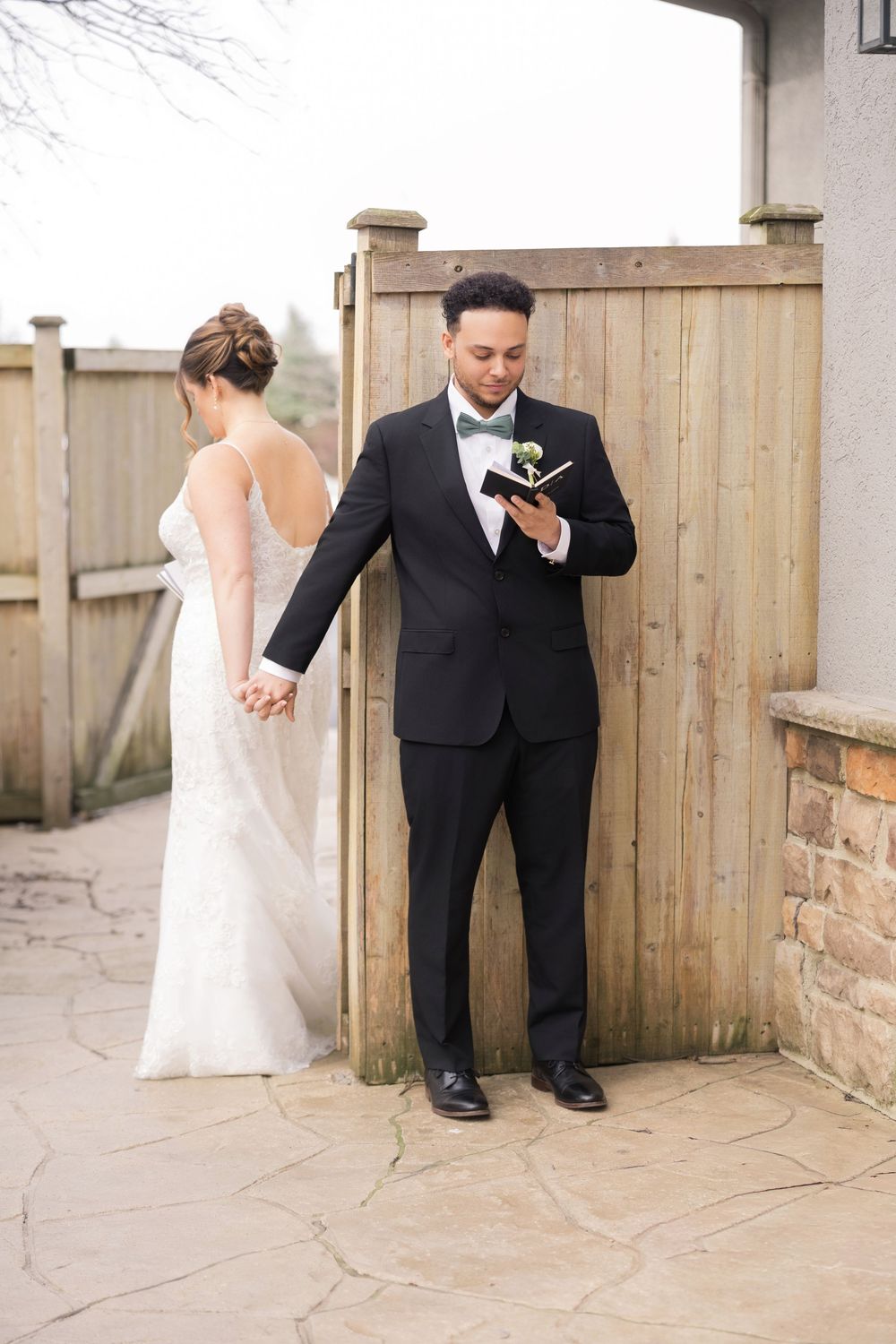 Bride and groom hold hands around wooden fence during emotional private vow exchange before ceremony.