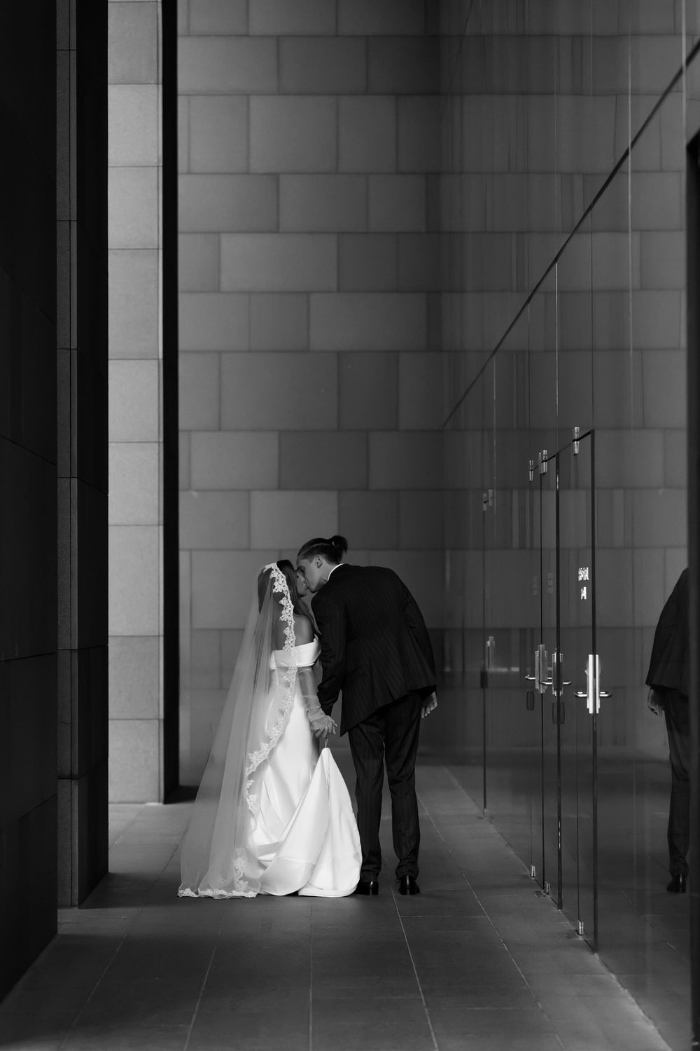 Black and white photo of a bride and groom sharing an intimate moment in a modern architectural hallway.