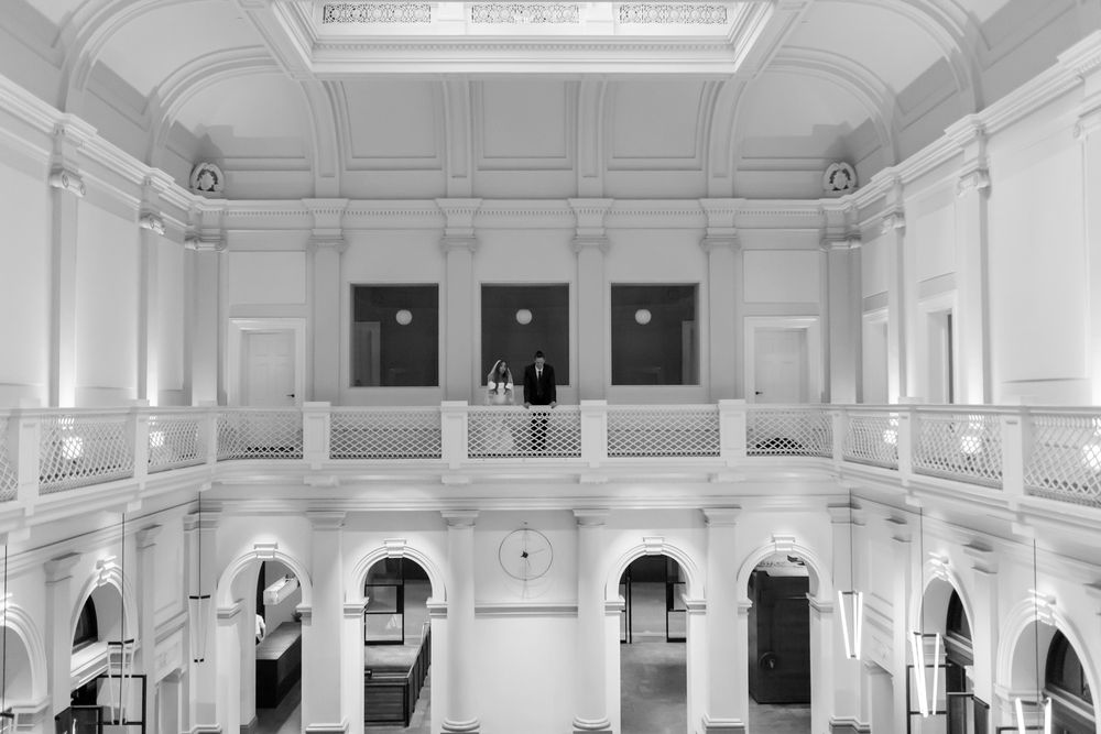 Black and white photo of elegant neoclassical building interior with balcony, arched windows, and ornate white moldings.