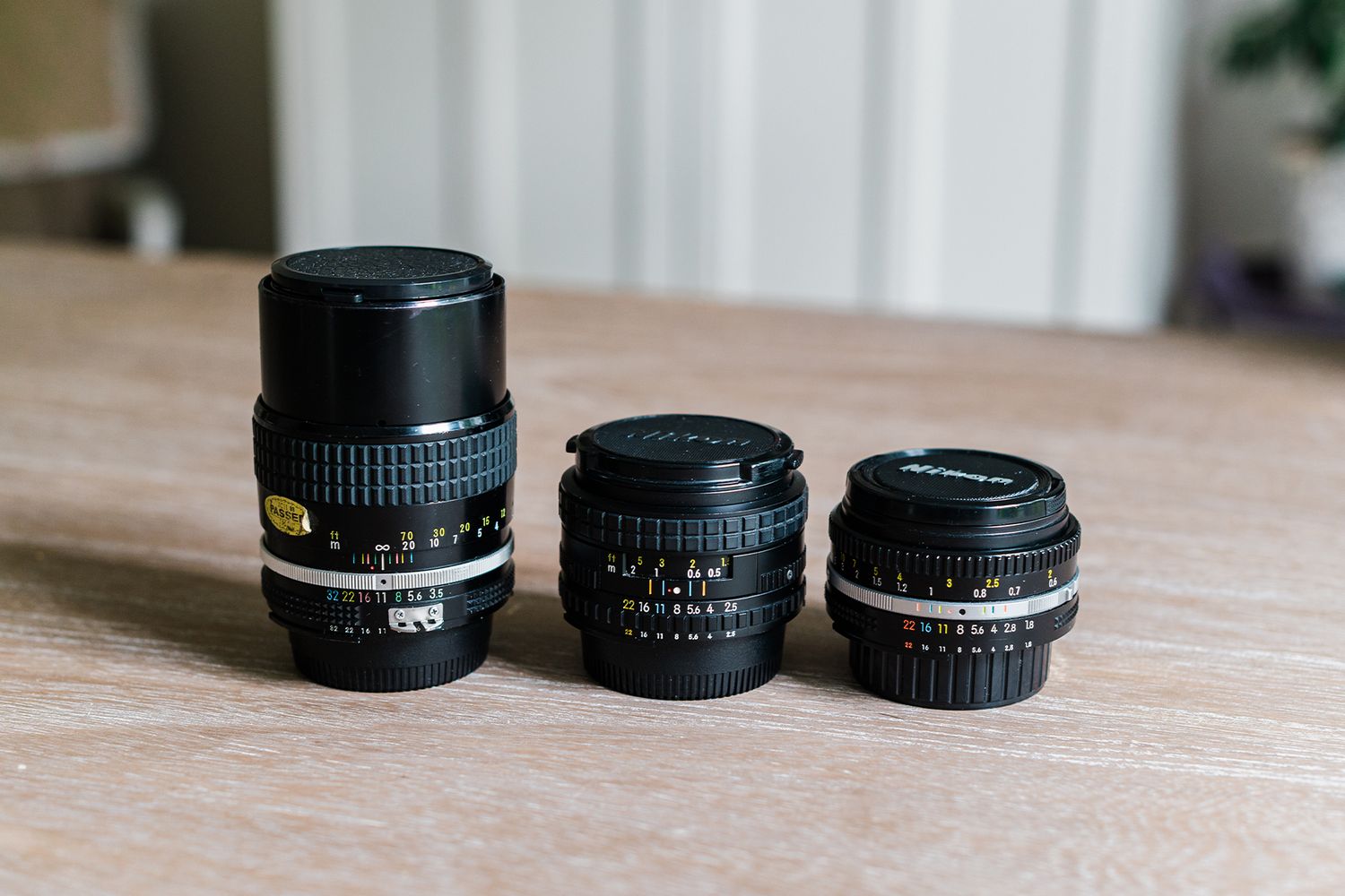 Three Nikon camera lenses of varying sizes arranged on a wooden surface, showcasing different focal lengths.