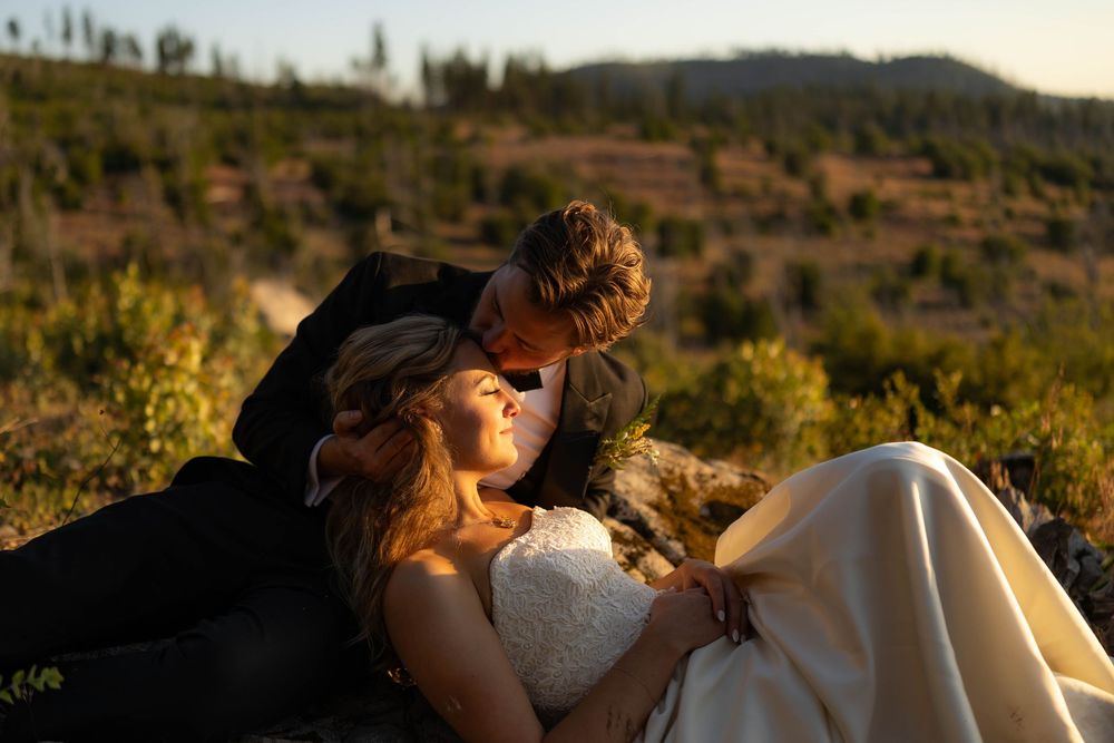 Bride and groom relax together in golden sunset light among lush mountain greenery.