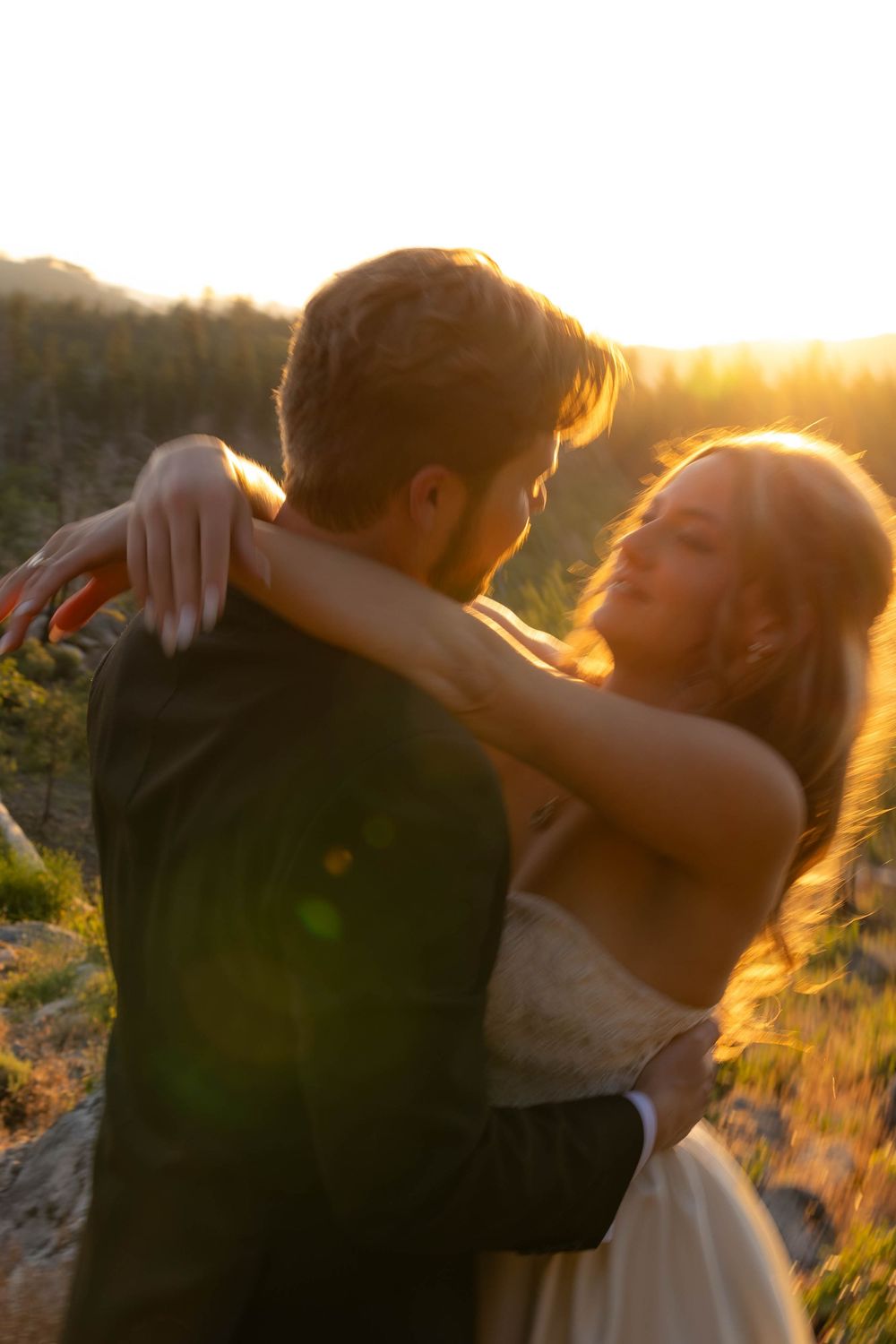 Bride and groom embrace romantically in warm golden sunset light in an outdoor field setting.