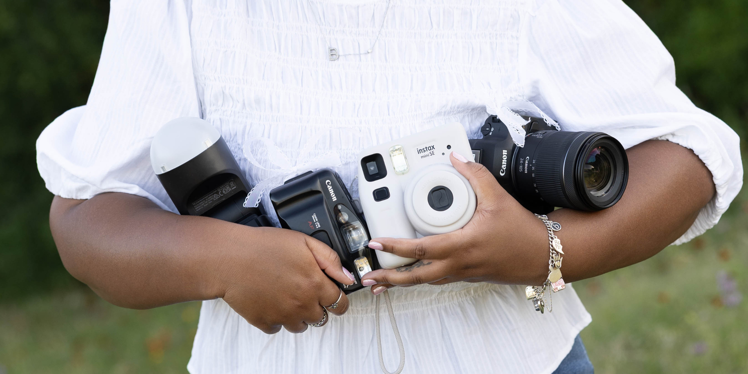 A Canon DSLR camera beside printed couple photos, film rolls, and SD cards on a wooden surface, held by a woman with red nails.