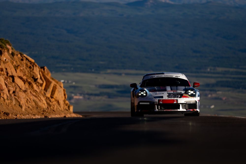 A race car speeds along a mountain road at Pikes Peak Hill Climb with scenic Colorado landscape in the background.