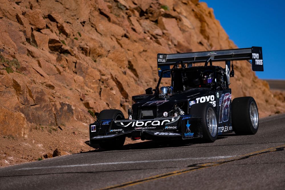Black Toyo Tires race car with large rear wing competing on Pikes Peak mountain road course.