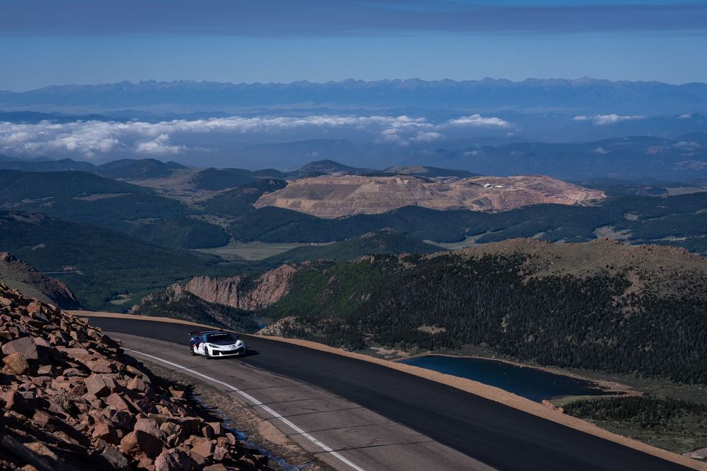 White car driving on a winding mountain road at Pikes Peak, Colorado, with stunning panoramic views and clouds below.