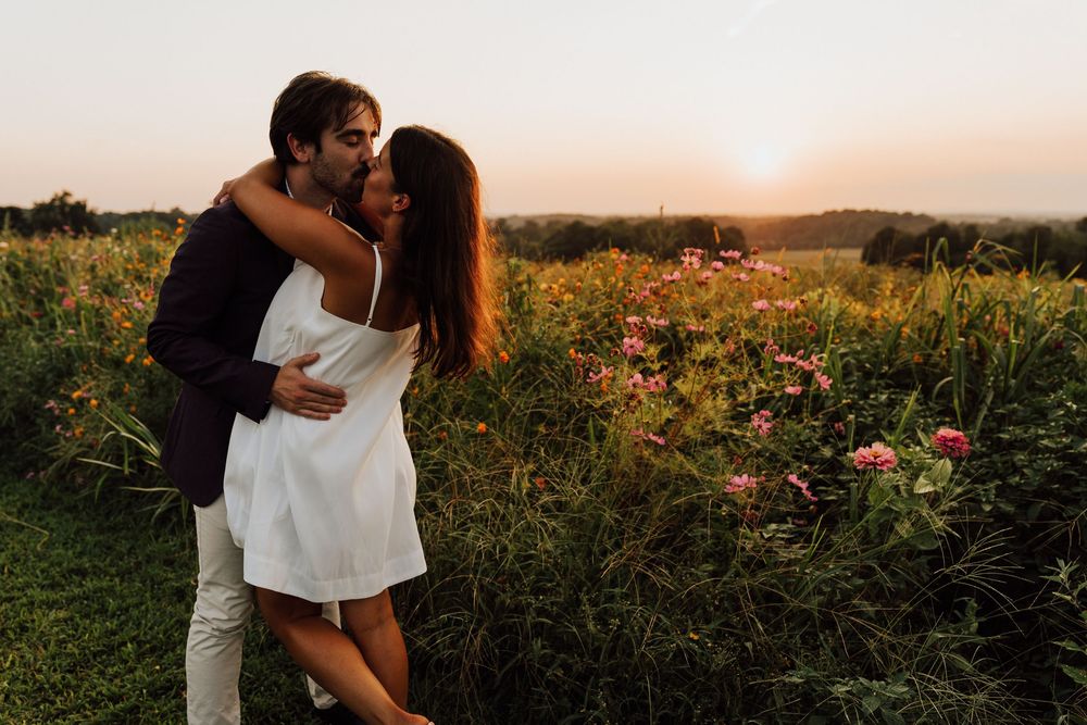 Romantic couple hugging in a flower field at golden sunset, woman in white dress.
