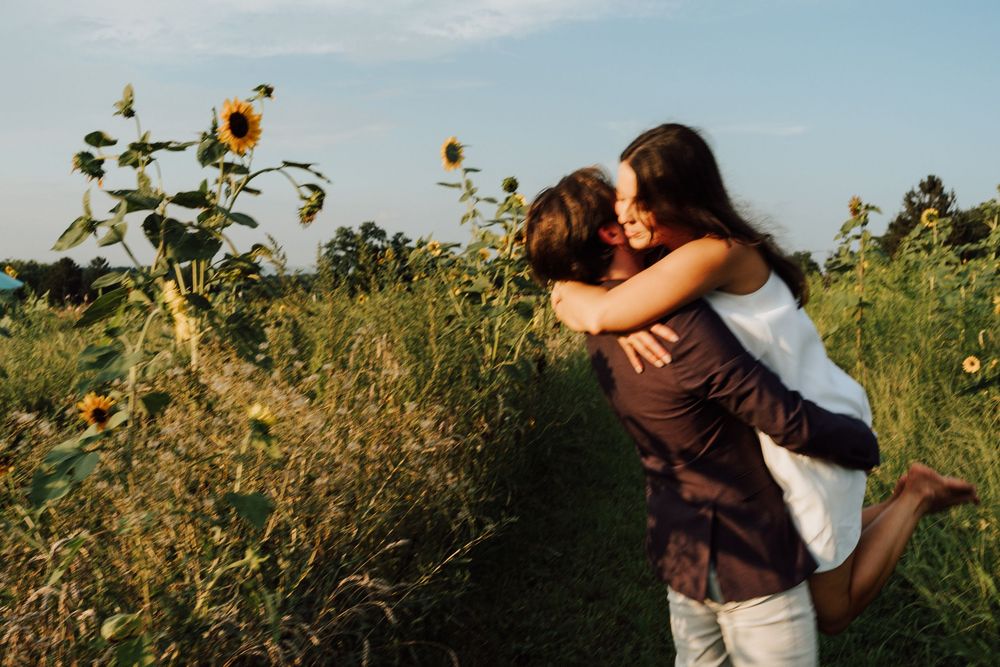 Joyful couple embracing and spinning near a sunflower field during a warm summer evening outdoors.