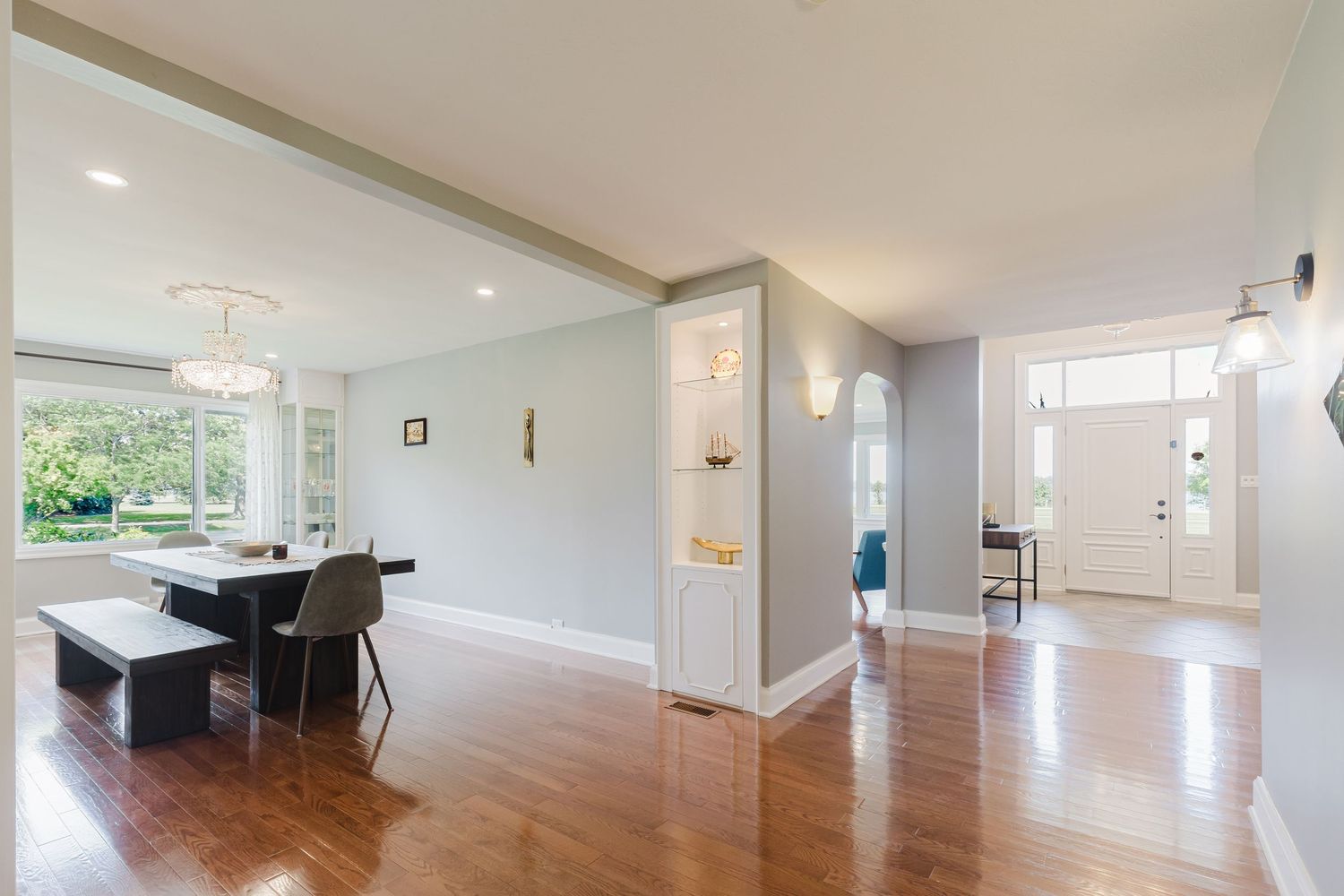 Bright open-concept living and dining area with hardwood floors, light gray walls, and a white front door.