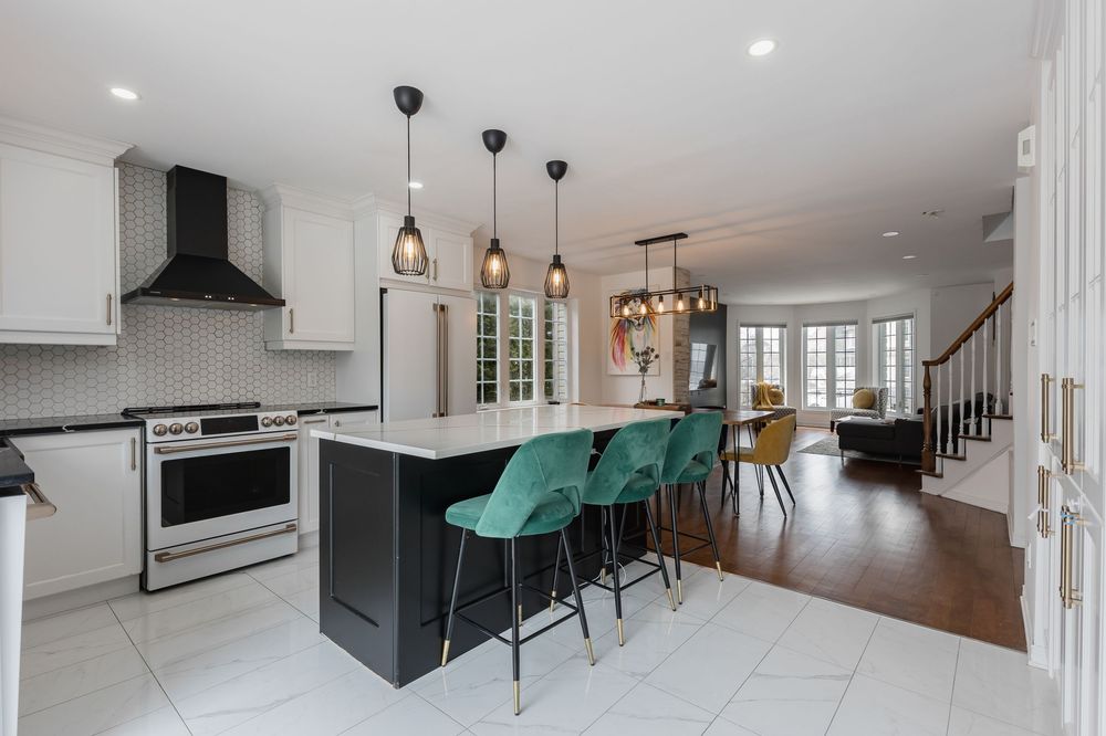 Modern kitchen with white cabinets, black island, green velvet bar stools, pendant lights, and stainless steel appliances.
