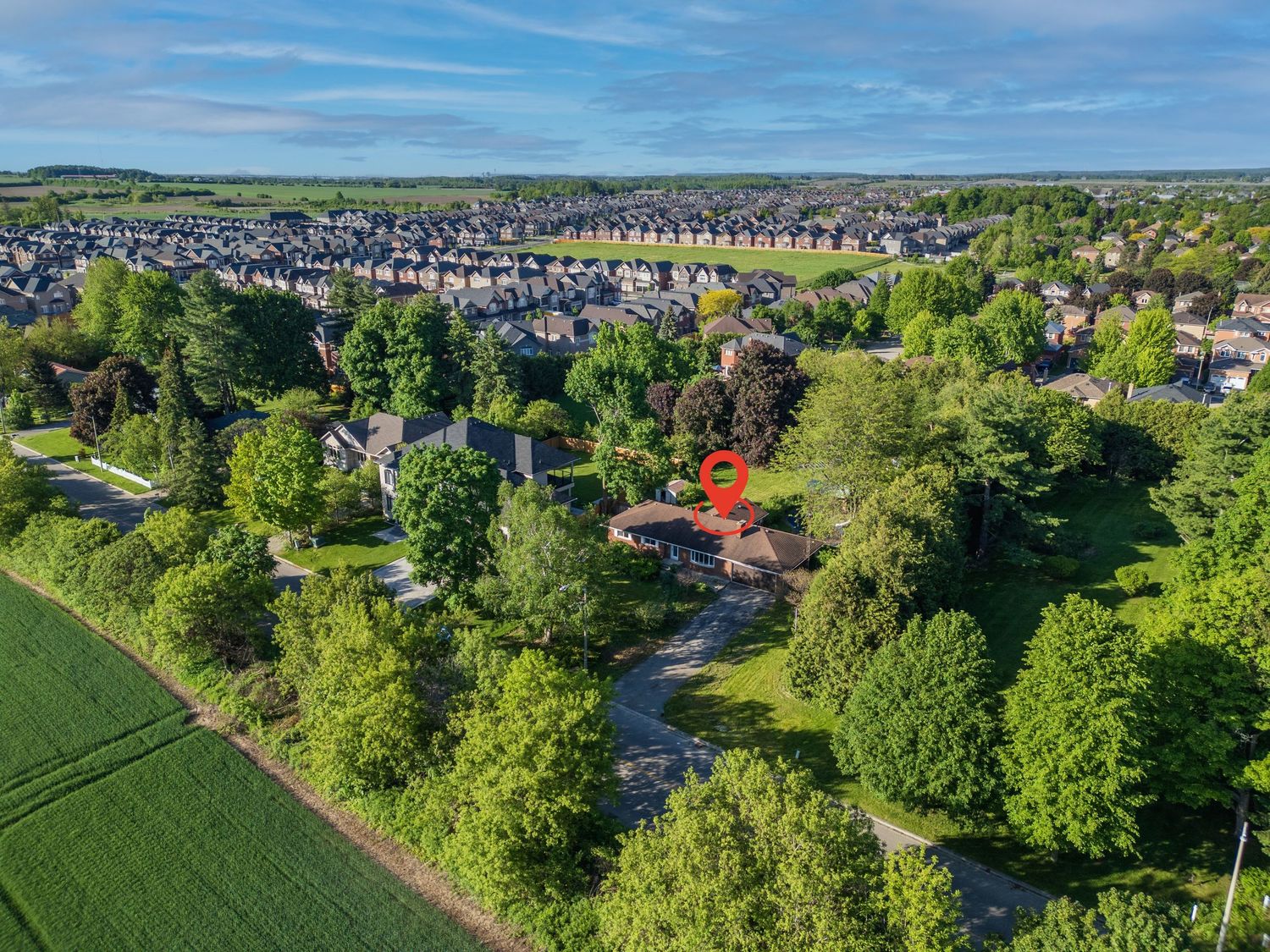 Aerial drone view of a secluded property surrounded by lush green trees with a residential neighborhood in the background.