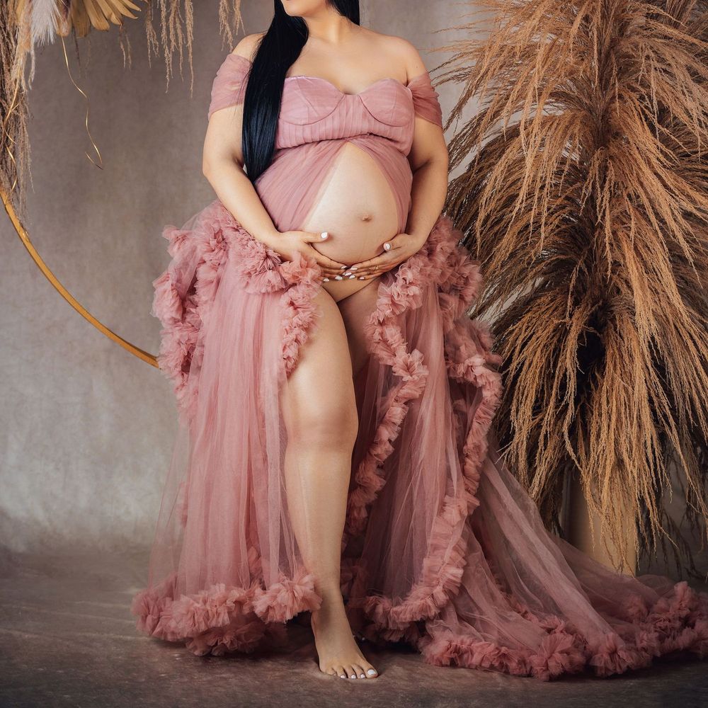 Pregnant woman in dusty rose tulle maternity robe gown, off-shoulder style, posing for a photoshoot.