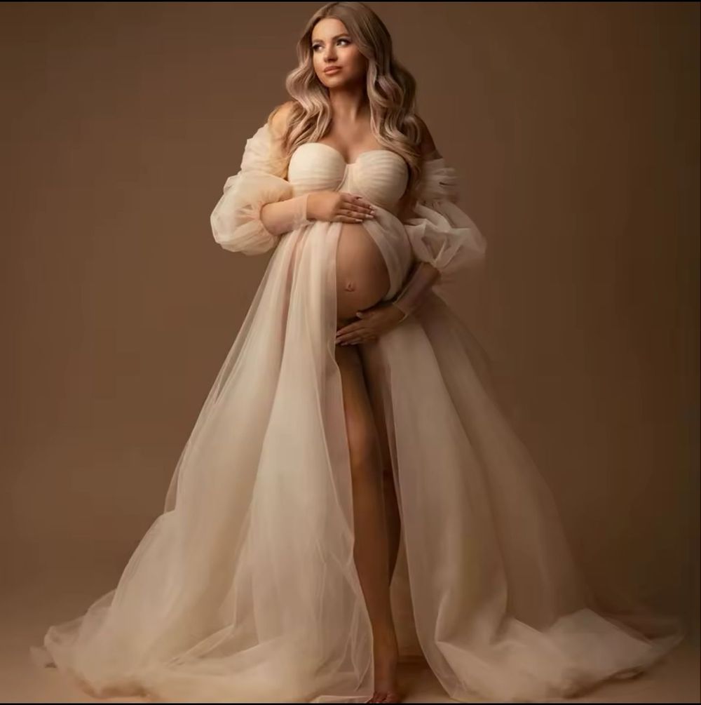 Pregnant woman in elegant champagne tulle maternity gown with puff sleeves and flowing skirt for photoshoot.